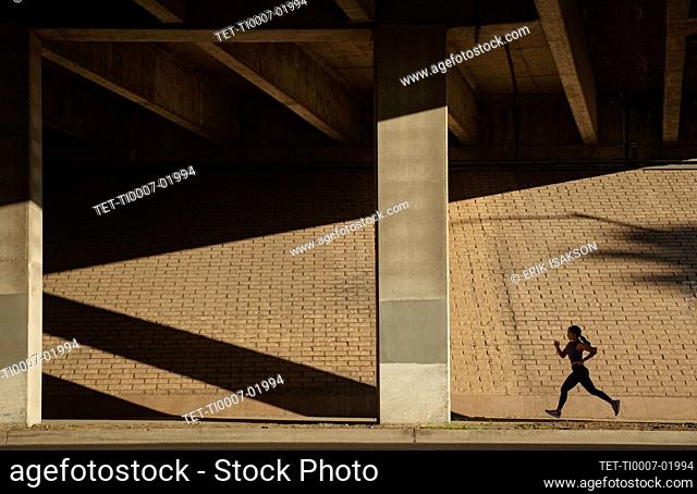 Woman jogging near brick wall in sunlight