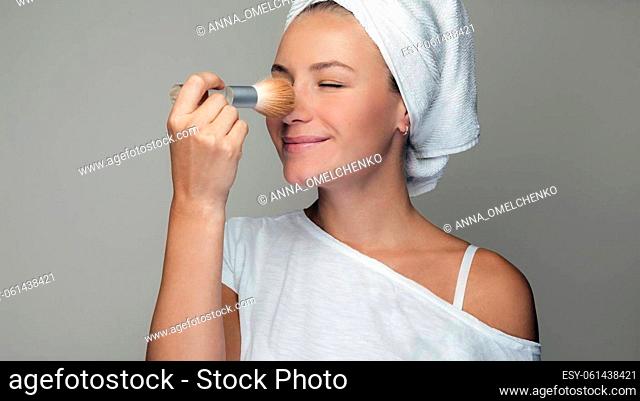 Portrait of a Nice Female After Bath Applying Makeup. Pretty Girl with Towel on her Hair Powdering the Face with a Brush. Beauty and Youth
