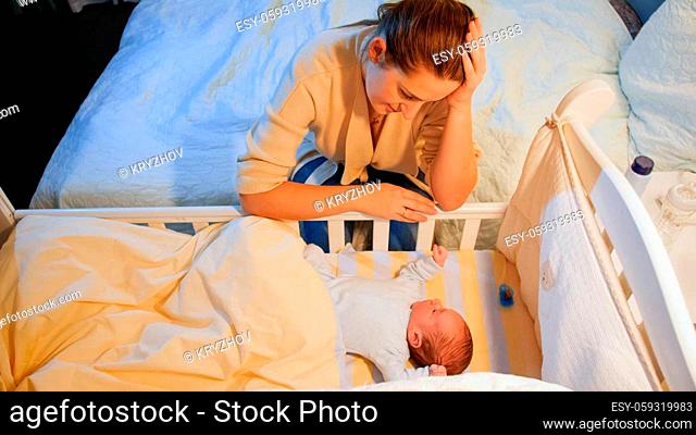 Exhausted young woman rocking crib of her sleepless newborn baby. Maternal depression after childbirth and sleepless nights