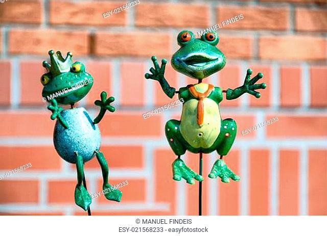 Kermett ähnliche Frosch-Skulptur, die mit seiner Prinzessin im Garten vor der Hauswand tront. Grüne Frösche vor Hintergrund aus roten Ziegelsteinen