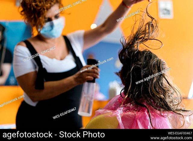 Female hairdresser spraying water on girl's brown hair at barber shop