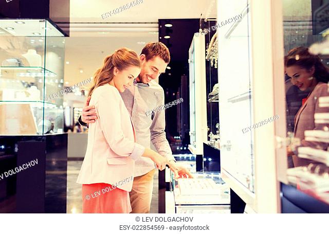 sale, consumerism, shopping and people concept - happy couple choosing engagement ring at jewelry store in mall