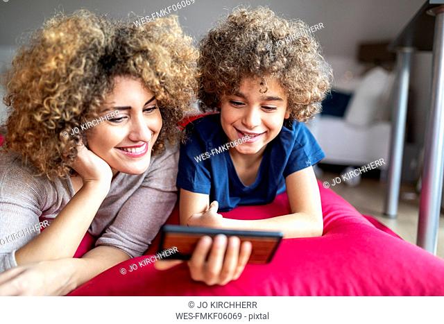 Mother and son watching a video on smartphone, lying on big pillow