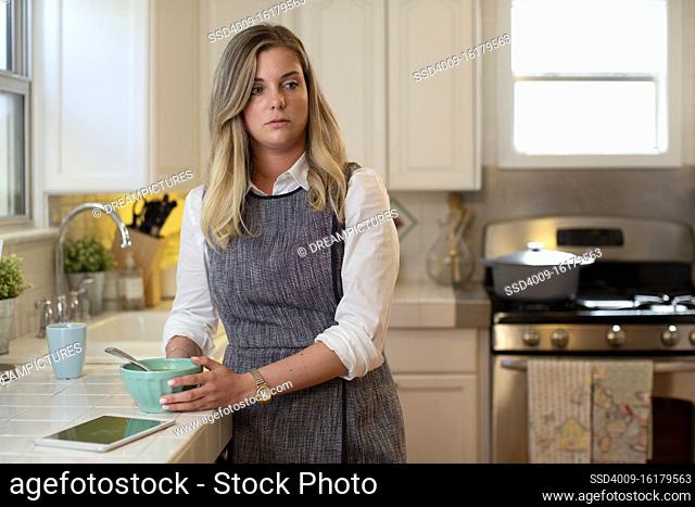 Young woman in her kitchen eating soup looking off camera