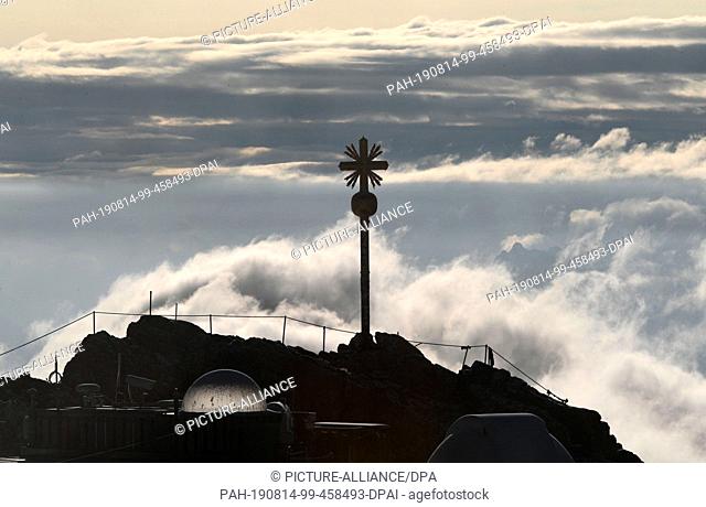 14 August 2019, Bavaria, Zugspitze: The summit cross of Germany's highest mountain can be seen from the tower of the Zugspitze weather station