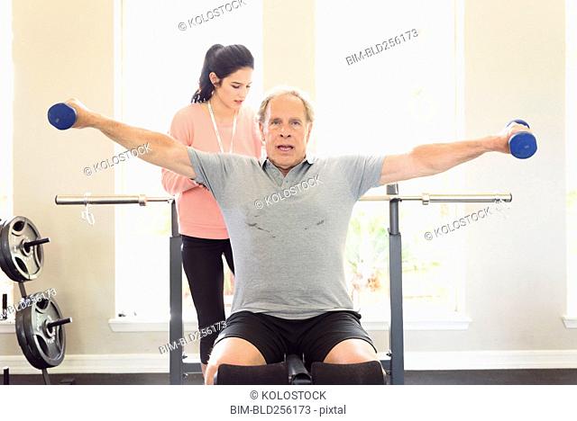 Caucasian trainer watching man lifting dumbbells