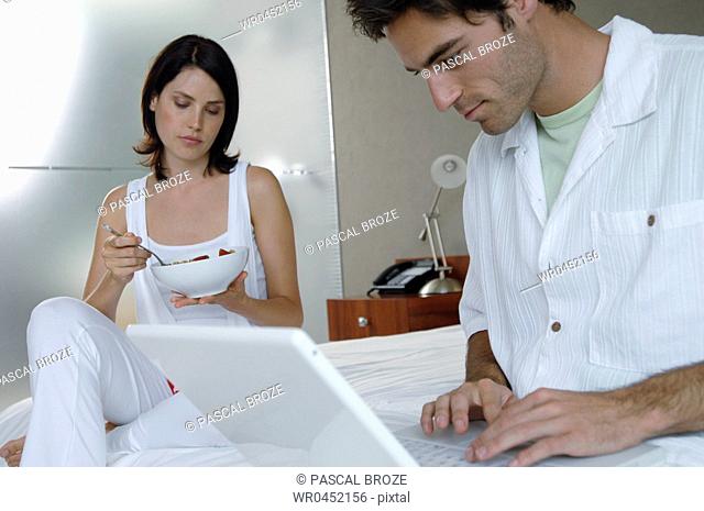 Mid adult man using a laptop with his wife holding a bowl of strawberry beside him