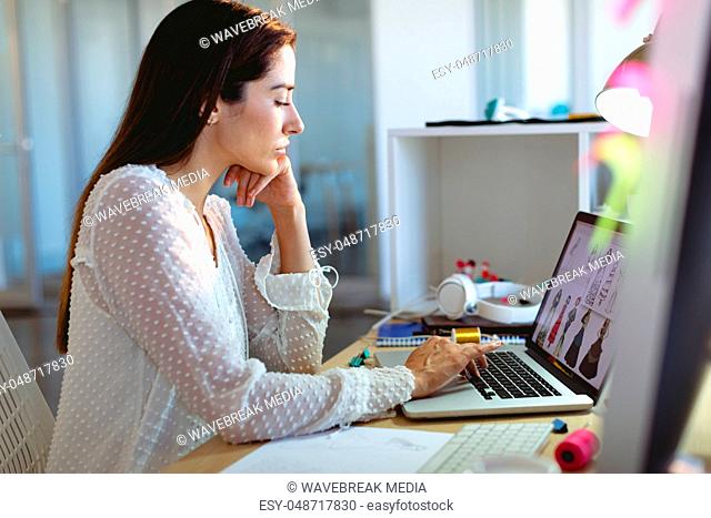 Female fashion designer working on laptop at desk in a modern office
