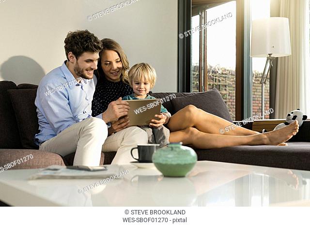 Parents and son sitting on sofa holding tablet at home