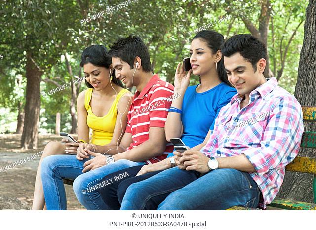 Friends using mobile phones and mp3 player in a park, Lodi Gardens, New Delhi, Delhi, India