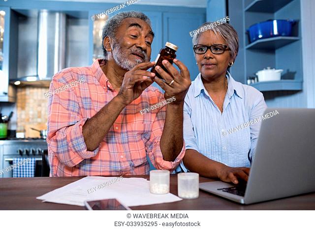 Man looking at medicine while sitting by woman using laptop