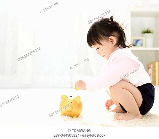 baby girl inserting a coin into piggybank