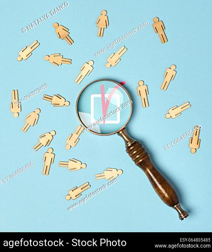 Wooden men and a magnifying glass on a blue background. Recruitment concept, search for talented and capable employees, career growth, flat lay
