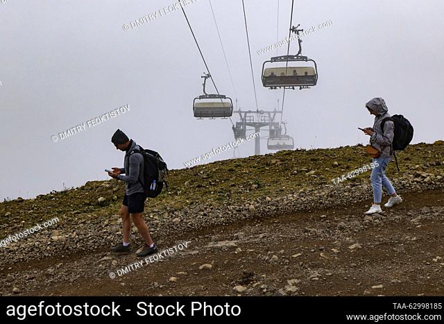 RUSSIA, SOCHI - OCTOBER 4, 2023: Holidaymakers walk under a chair lift in the Rosa Khutor mountain resort in the Caucasus Mountains in mid-autumn