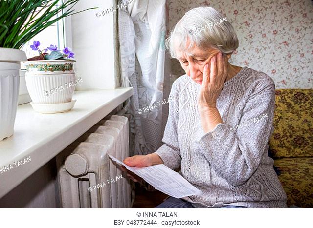 The senior woman holding gas bill in front of heating radiator. Payment for heating in winter