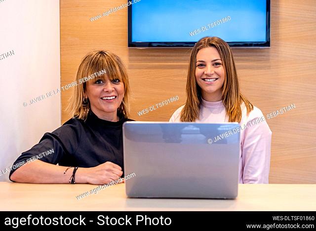 Female dentist and receptionist smiling while sitting in front of laptop at desk