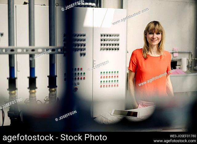 Smiling female entrepreneur standing against control panel in greenhouse