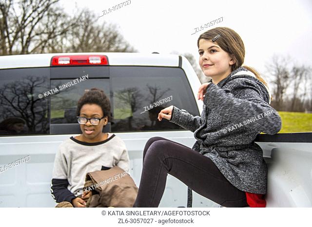 Two teens/ Pre-teens having fun in the back of a pick up truck. They are outdoor and sitting inside the truck. . One African American teen girl