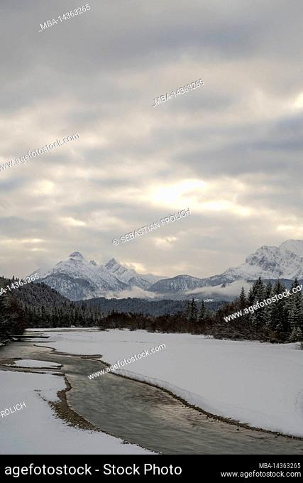 The course of the river Isar at the Wallgauer Isarsteg in winter with snow and thick clouds. In the background the Arnspitze and on the right the Wetterstein...