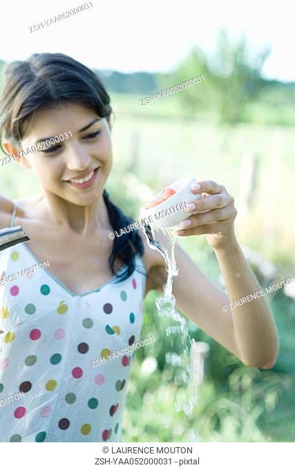 Young woman rinsing tomatoes in cup outdoors