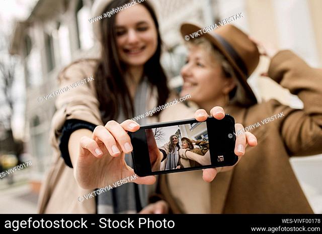 Daughter showing her selfie with mother on smart phone screen