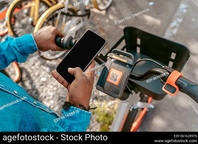 Mobility. Top view of dark-skinned male hand holding smartphone with screen on camera over bicycle handlebar outdoors no face