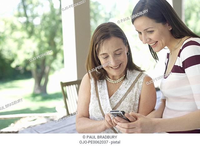 Two women outdoors on patio using personal digital assistant and smiling