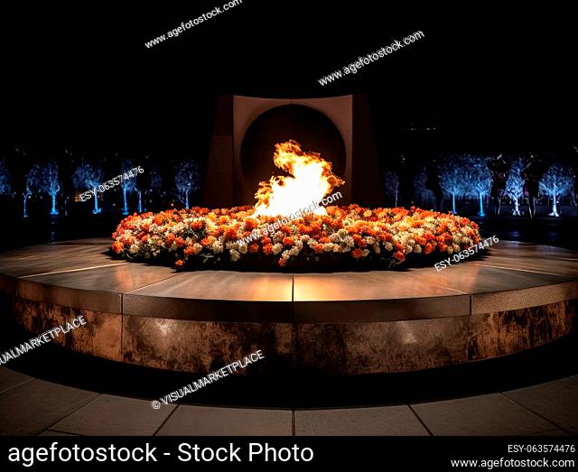 A striking image of the eternal flame burning brightly against the dark canvas of the night sky. The monument it illuminates is adorned with an array of flowers