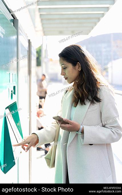Young woman using ticket machine at tram stop