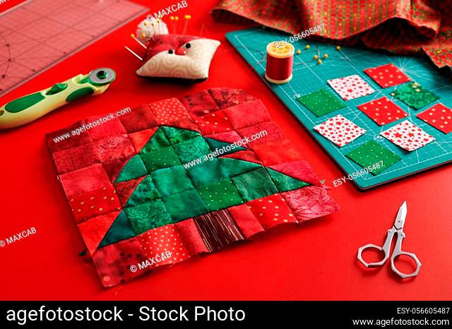 Christmas tree patchwork block, craft mat, bright square pieces of fabric, pincushion like Santa and quilting accessories on red background