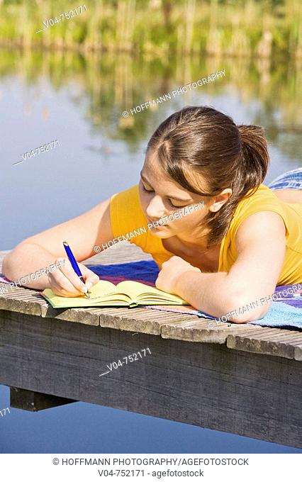 Teenaged girl writing in her diary outdoors looking thoughtful