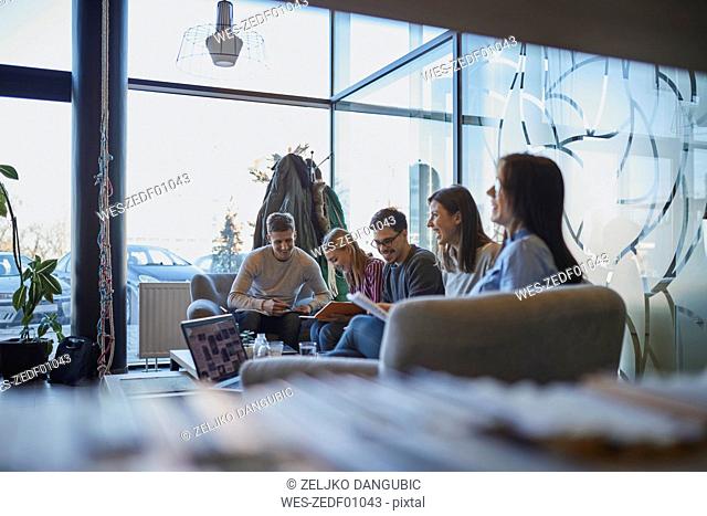 Group of happy friends sitting together in a cafe with laptop and documents