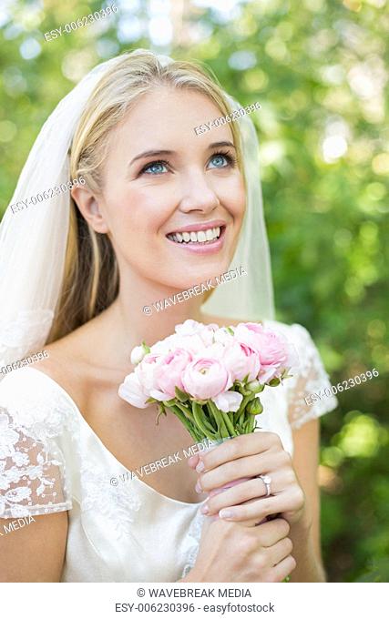 Smiling bride holding her bouquet wearing a veil looking up