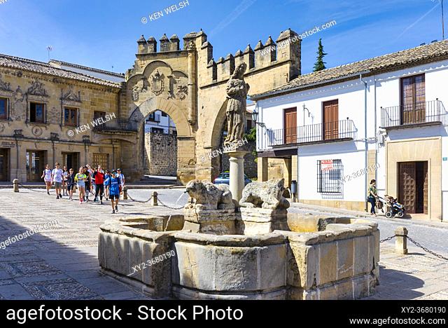 Fuente de los Leones, or Fountain of the Lions, in the Plaza del Populo, Baeza, Jaen Province, Andalusia, Spain. The ornamental city gate in the background is...