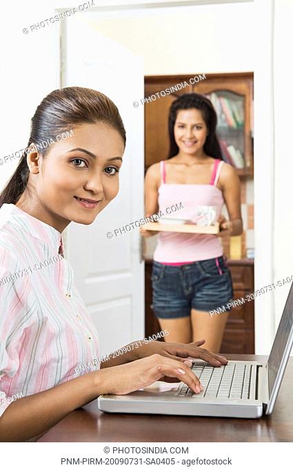 Woman using a laptop with her girlfriend serving coffee
