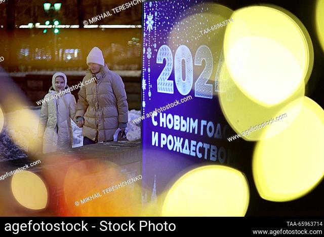 RUSSIA, MOSCOW - 21 de diciembre de 2023: Una mujer lleva a una chica a mano pasando un cartel de la calle de Navidad. Mikhail Tereshchenko/TASS
