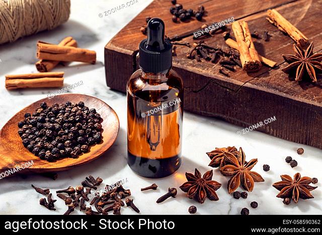Aromatic seeds essential oil on glass bottle. Cinamon, anise, peppercorn, clove oil for weelness, spa, aromatherapy