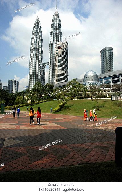 Petronas Twin Towers seen across park with the round dome of the Asy-Syakirin mosque seen to right grass and trees around mosque with people walking along red...