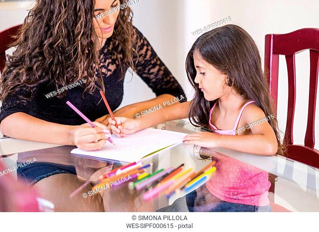 Teenage girl drawing with her little sister at table