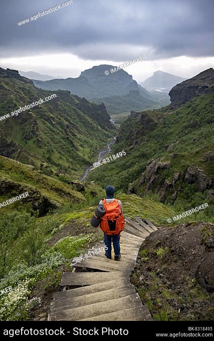 Hikers on hiking trail with steps, mountain landscape with river valley, in the back mountain valley with river Krossá and mountain Valahnúkur