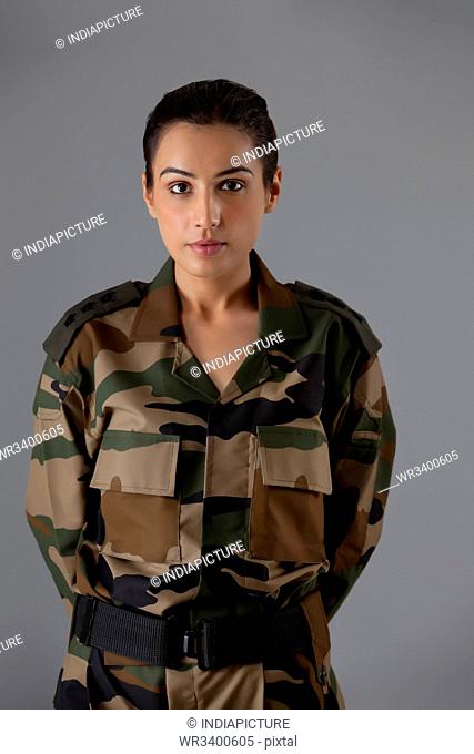 Portrait of young female soldier standing against colored background