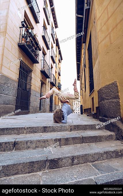 Young woman practicing yoga in the city, performing forearm stand in the street