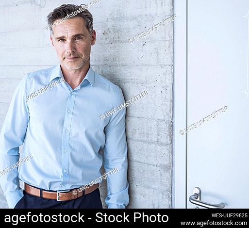 Smiling businessman leaning on wall in office