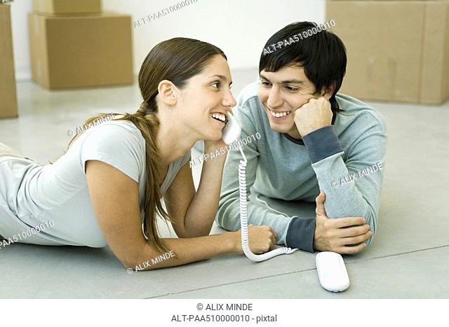 Couple lying on the floor, woman talking on landline phone, boxes in background