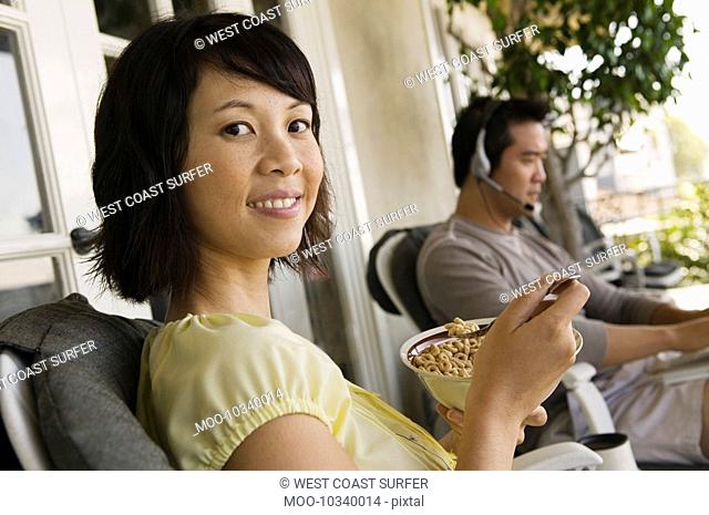 Woman having breakfast on porch man using laptop in background