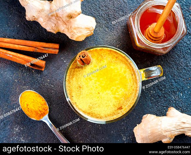 Healthy drink golden turmeric latte in glass cup.Gold milk with turmeric, ginger root, cinnamon sticks, turmeric powder and honey on black background