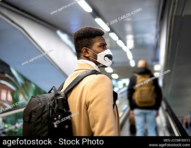 Young man wearing face mask standing on escalator at station