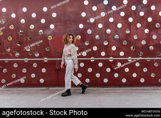 Young blond woman walking by maroon metallic wall
