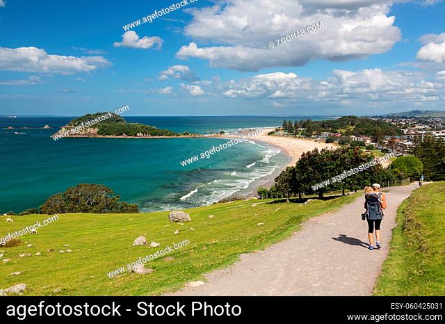 Woman with baby in carrier hikes the steep path around the Mount in Tauranga New Zealand