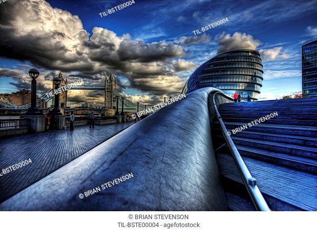 More riverside along the south bank in southwark in london with the city hall and tower bridge and a cloudy dramatic blue sky as a backdrop